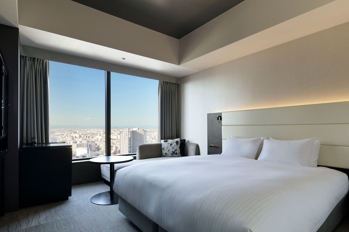 Une chambre d’hôtel avec un grand lit, un bureau, une chaise et une vue sur le paysage urbain.