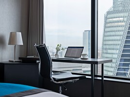 Une chambre d’hôtel moderne équipée d’un bureau, d’un ordinateur portable et offrant une vue sur le paysage urbain.