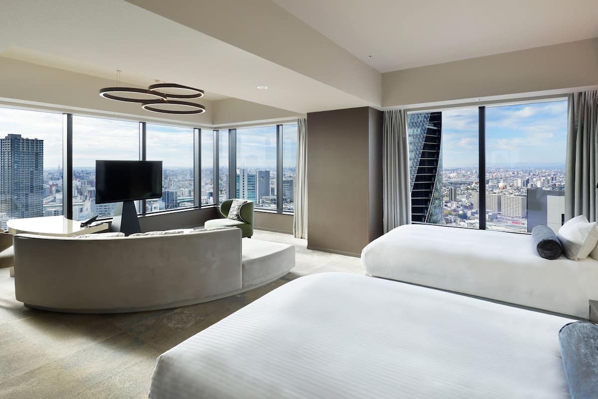 Une chambre d’hôtel moderne dotée d’un espace salon aux lignes courbes, d’un lit et d’une grande fenêtre donnant sur la ville.