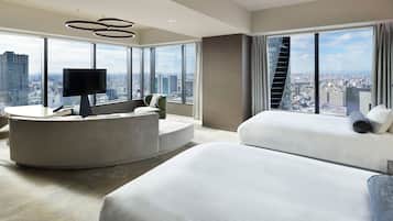 A modern hotel room with a curved seating area, a bed, and a large window offering a city view.