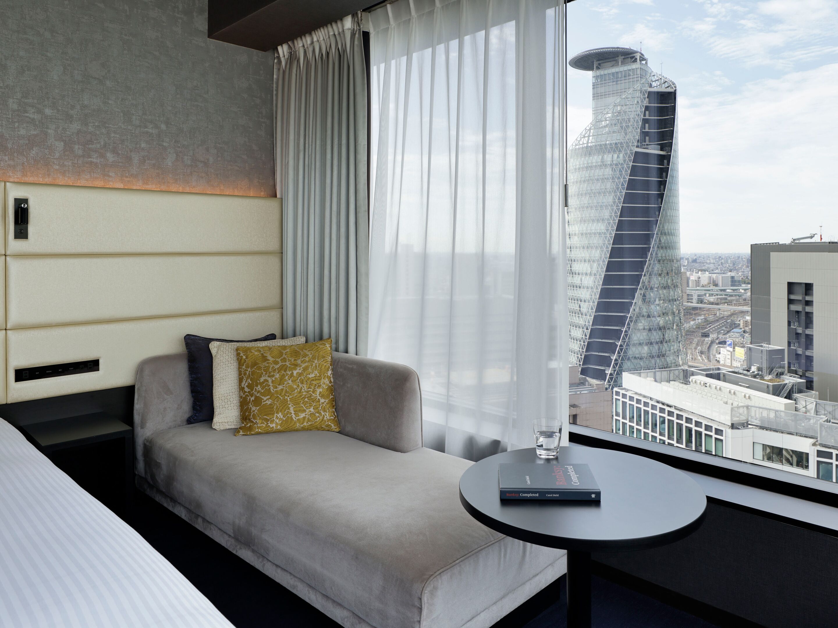 A modern hotel room with a sofa, a small table, and a view of a cityscape.