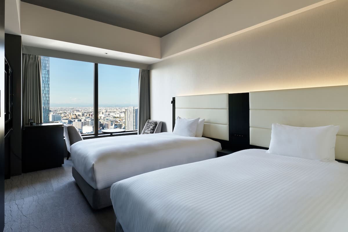 Une chambre d’hôtel avec deux lits, un bureau et une grande fenêtre donnant sur la ville.