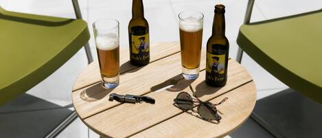 Uma mesa de madeira redonda com duas garrafas de cerveja, dois copos de cerveja, um par de óculos de sol e um abridor de garrafa.