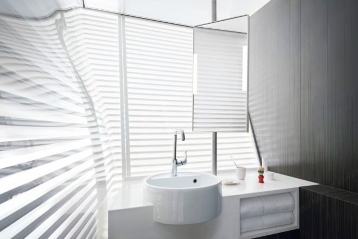 Een moderne badkamer met een witte wasbak, een grote spiegel en een raam met horizontale zonwering.