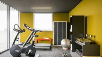 Una palestra con attrezzature per esercizi, una panca rossa, una palla grande da ginnastica e uno scaffale a parete con manubri.