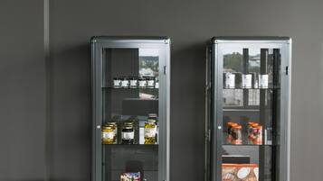 Two glass-fronted display cases with various food items, a red suitcase, and a black bag against a dark wall.