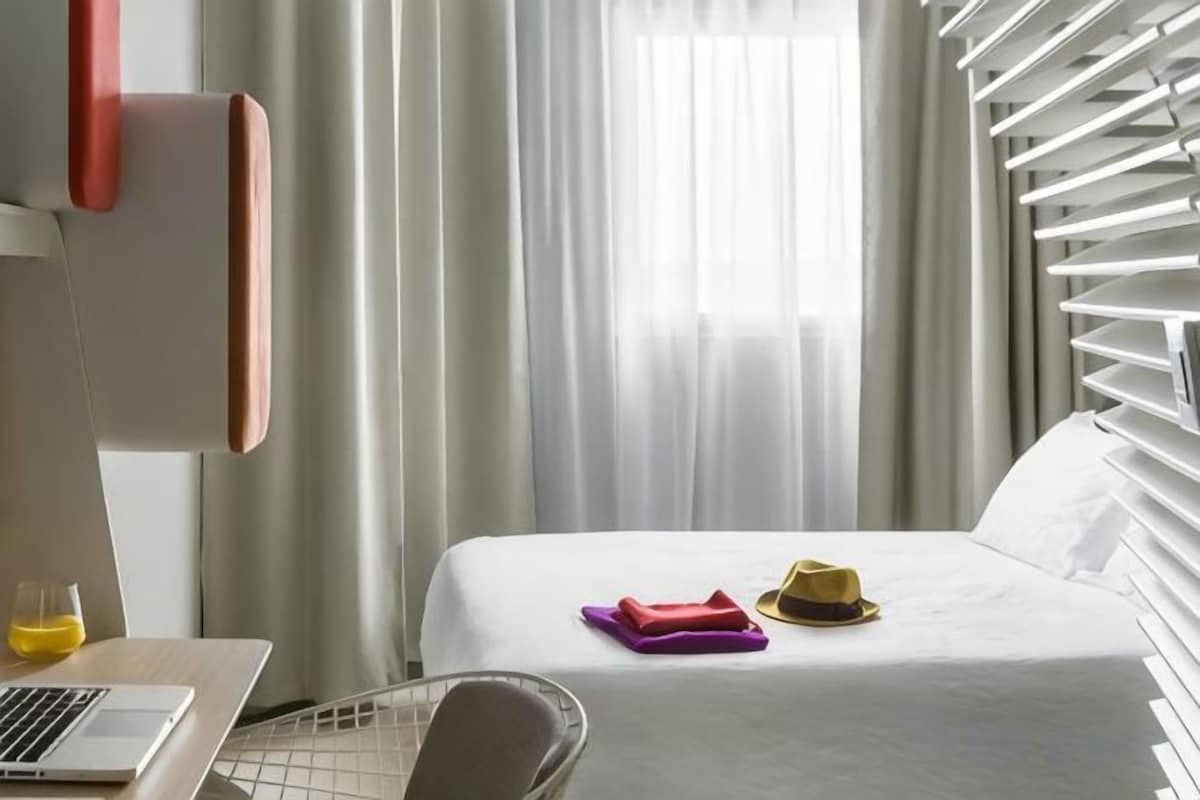 A hotel room with a bed, a desk with a laptop, and a chair.