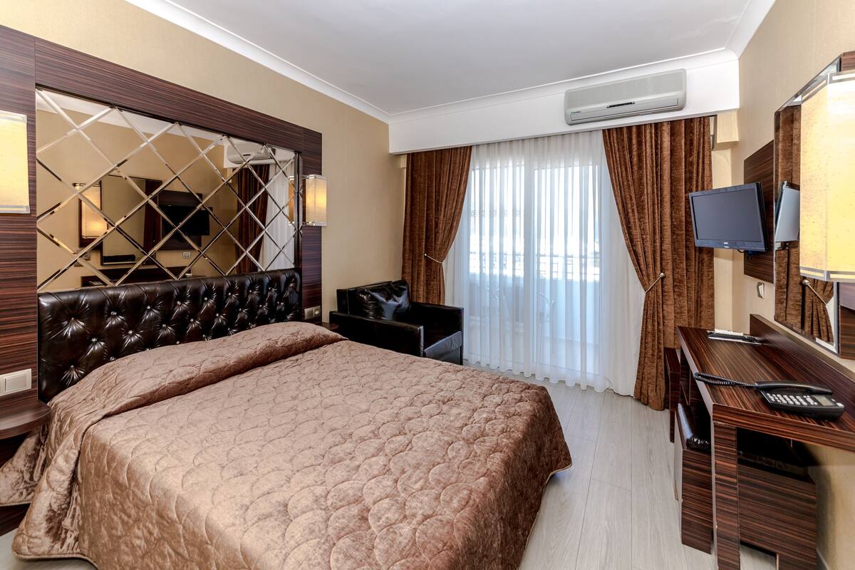 A hotel room with a large bed, a desk with a chair, a television, and a window with curtains.
