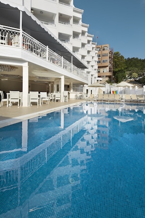 Ein Pool mit Sonnendeck, Liegestühlen und einem Gebäude mit Balkonen im Hintergrund.