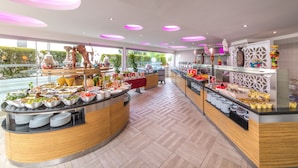 A modern buffet with various food stations, a decorative centerpiece, and a view of greenery outside. - Piccolo Dream Hotel - All Inclusive - Adults Only (Marmaris)