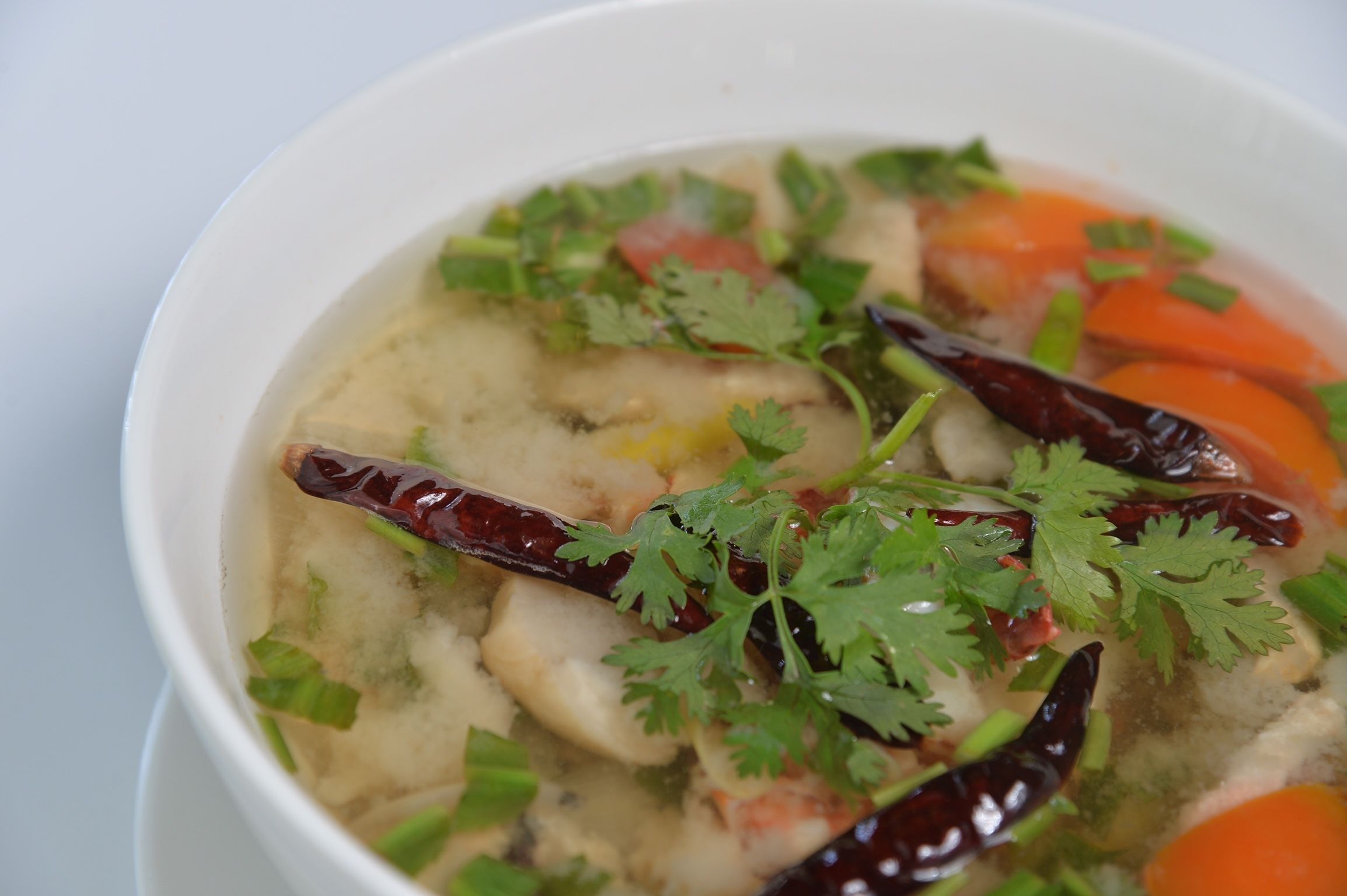 A bowl of soup with visible ingredients like carrots, herbs, and possibly mushrooms.