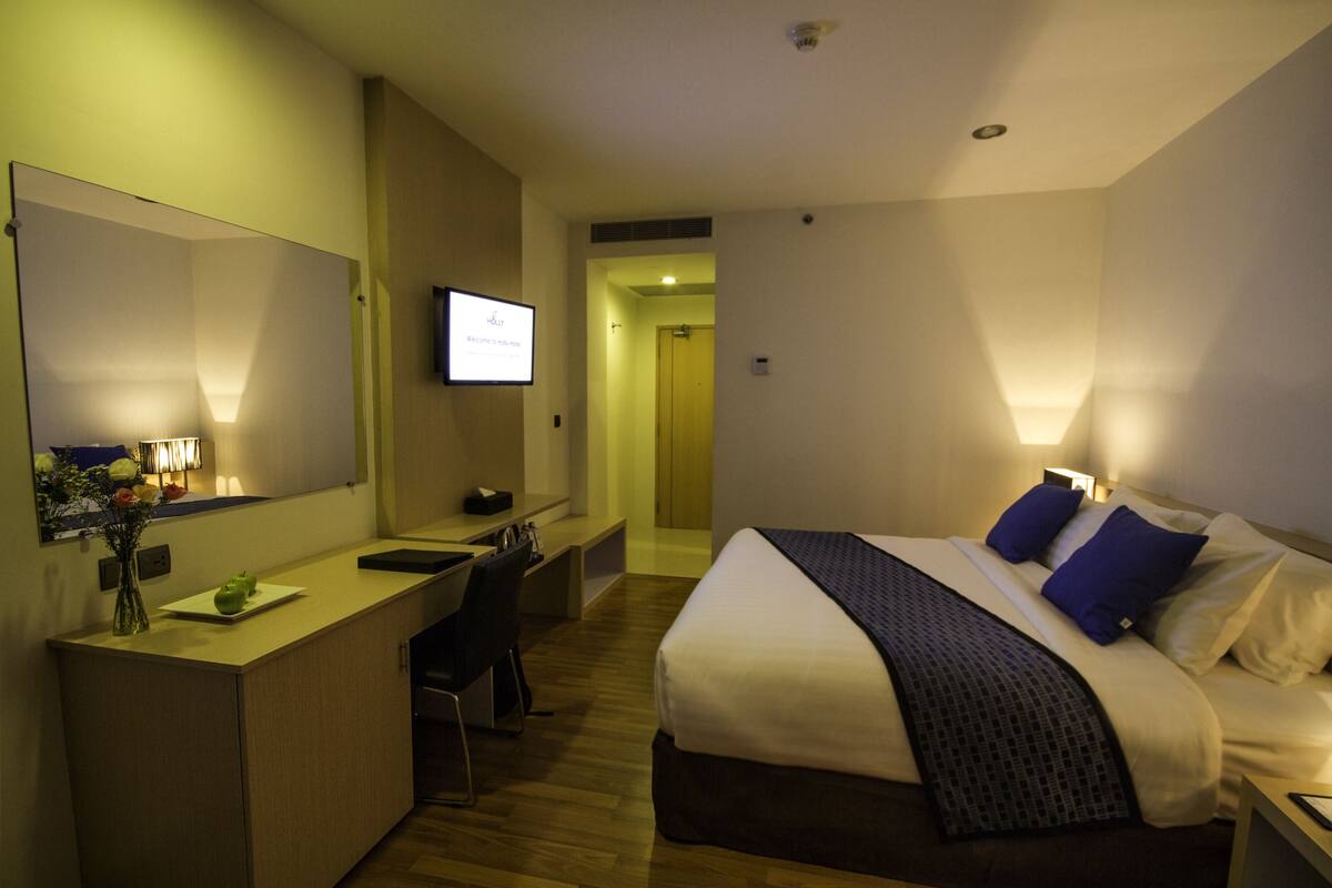 A hotel room with a bed, bedside table, desk, chair, and a large mirror.