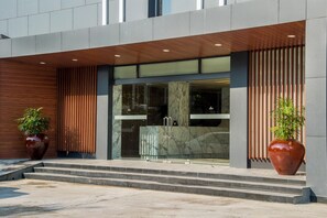 A modern building entrance with a glass door, steps, and two large potted plants. - Holly Hotel Myanmar (Yangon)