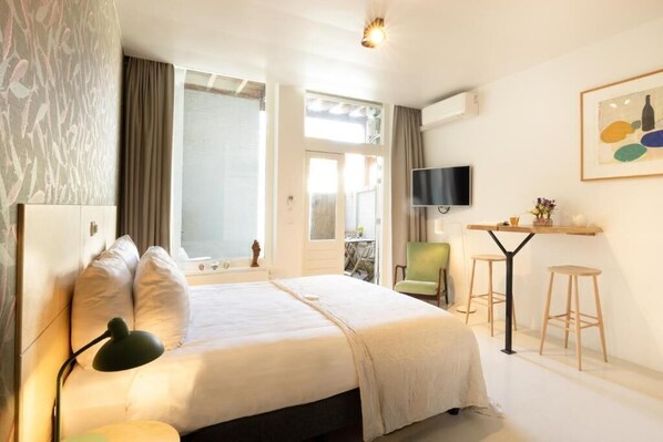 Une chambre d’hôtel avec un lit, un bureau et une chaise, une télévision et une fenêtre avec des rideaux.