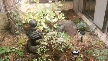 Un jardín con una estatua de piedra, diversas plantas y un pequeño estanque.