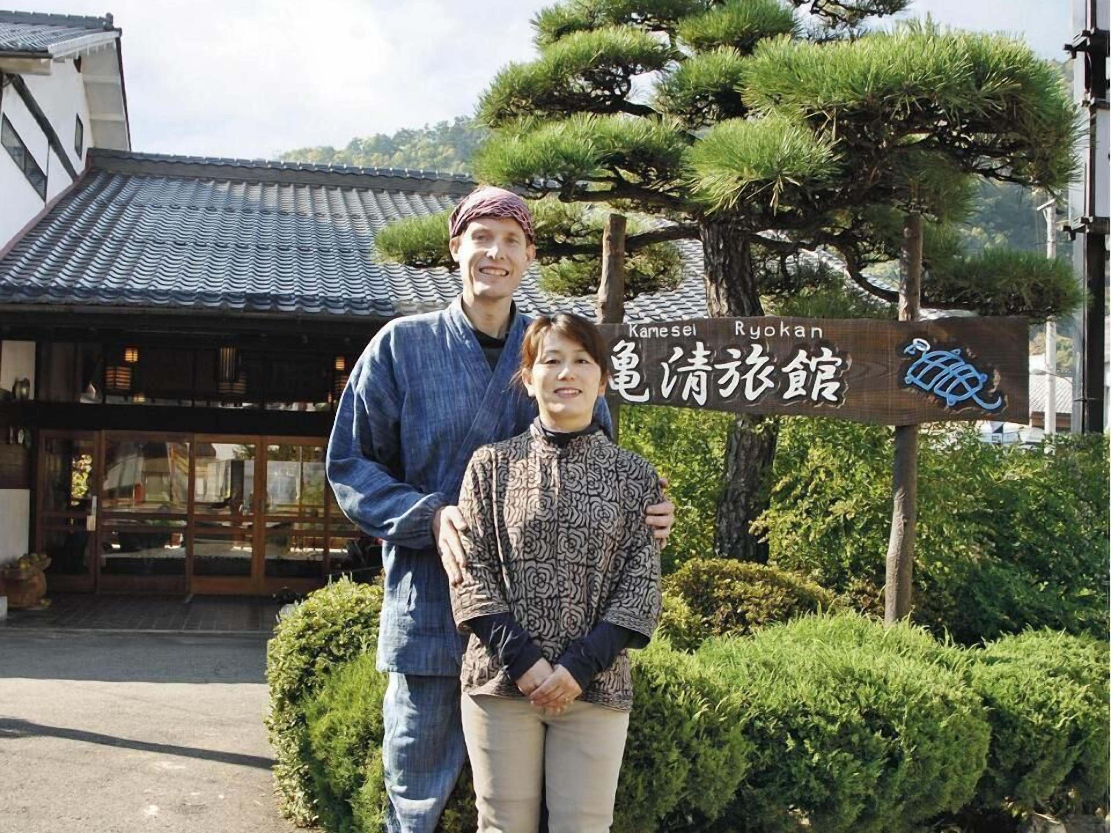 En traditionell japansk byggnad med ett tak täckt av tegelpannor och en skylt som visar att det är Kamesei Ryokan.