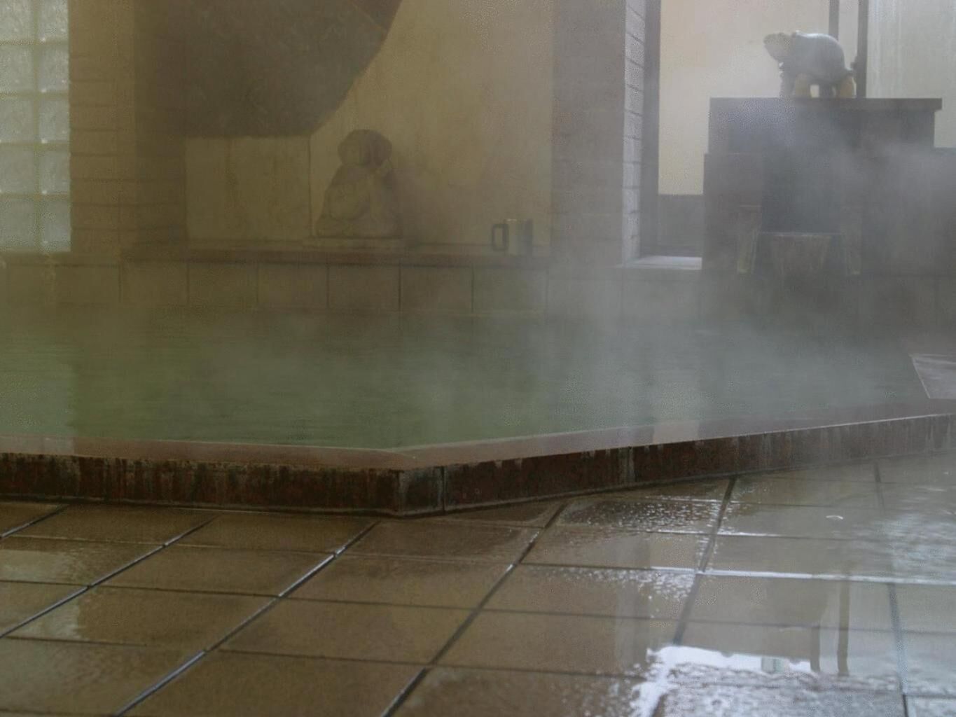 A steam room with a tiled floor and a person sitting in the steam.