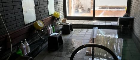 A wet bathroom with a tiled floor, a yellow shower head, and a window with a view of a wooden fence.