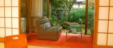 Um quarto em estilo japonês tradicional, com tatames, um sofá, uma poltrona de couro e uma mesa de vidro.