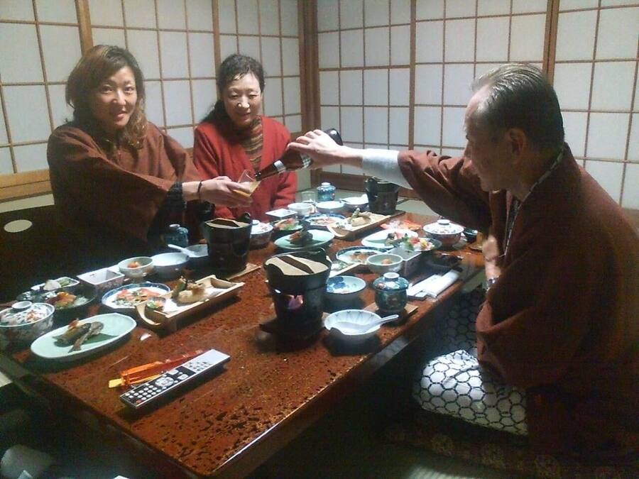 A group of people sitting around a table with various dishes and a remote control.