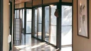 A corridor with large glass doors and windows, wooden ceiling, and a framed artwork on the wall.