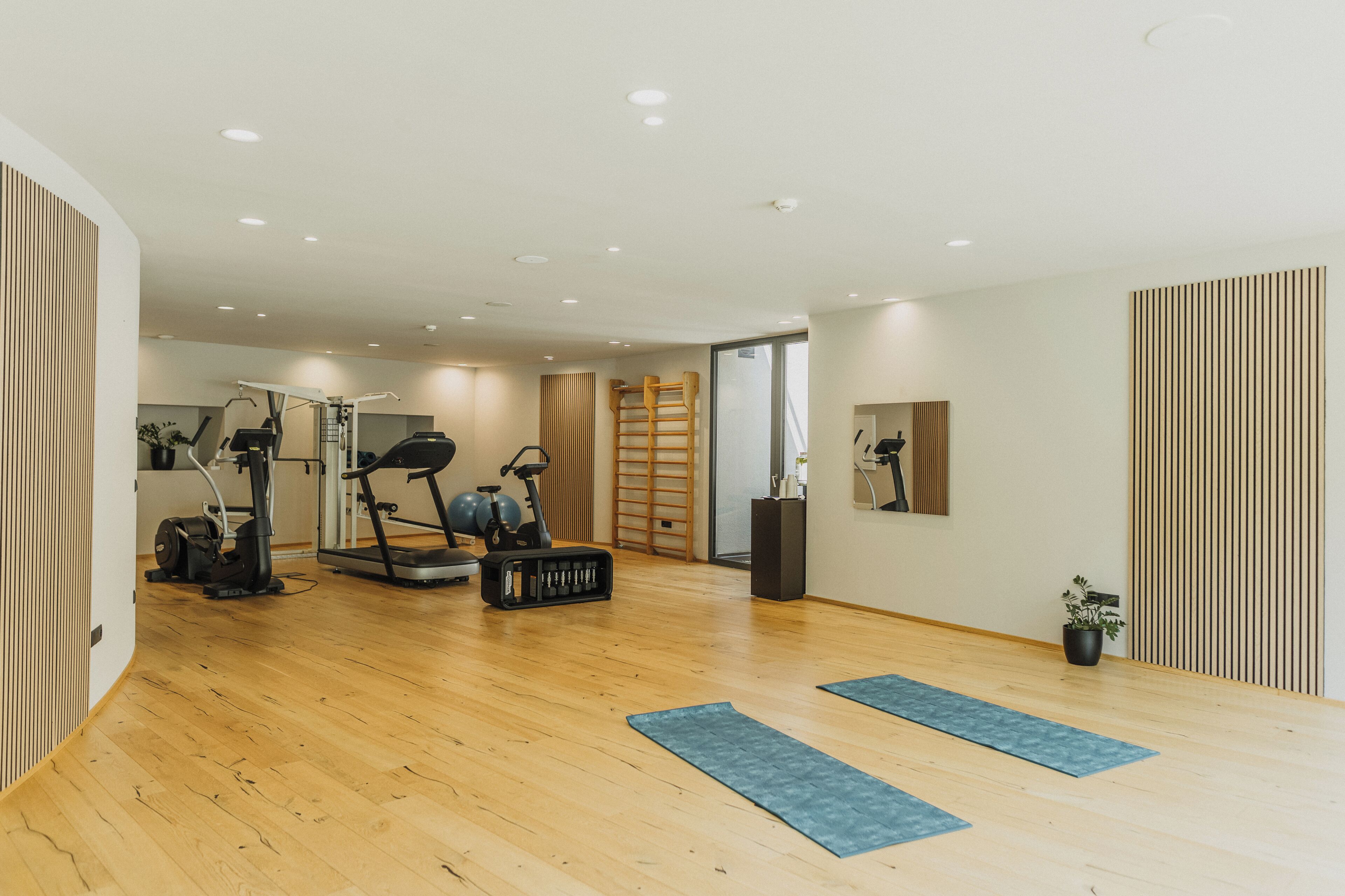 A spacious room with wooden flooring, exercise equipment, and a large window.