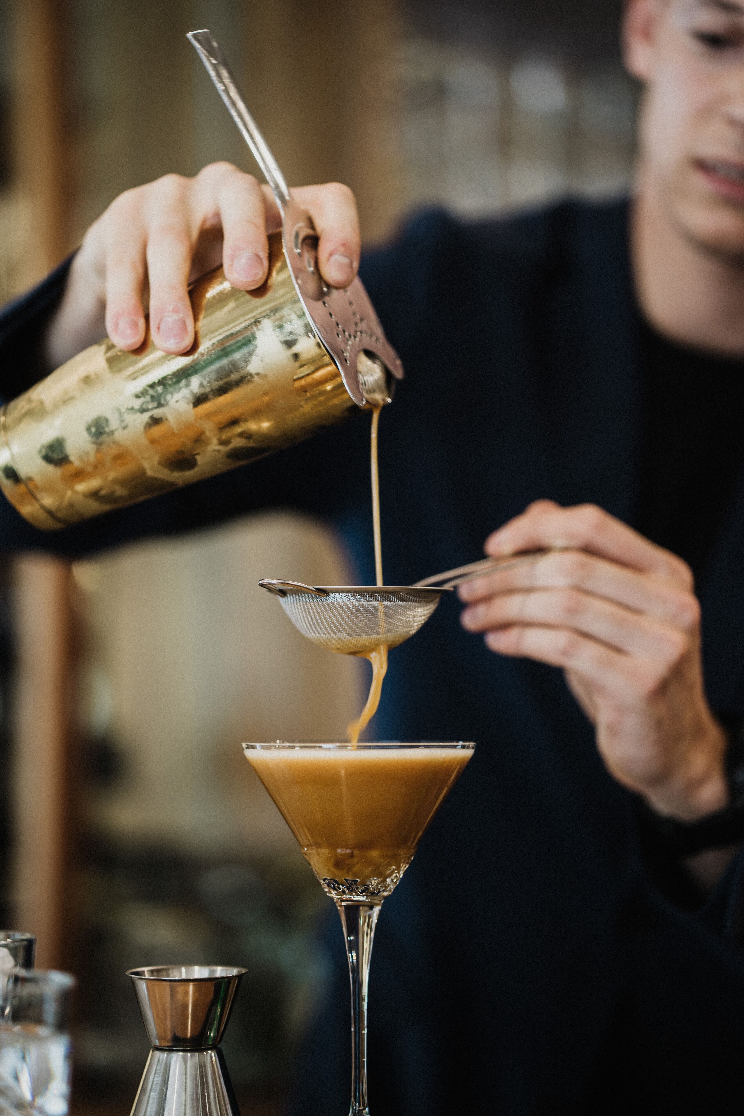 A person pouring a liquid into a martini glass using a strainer.