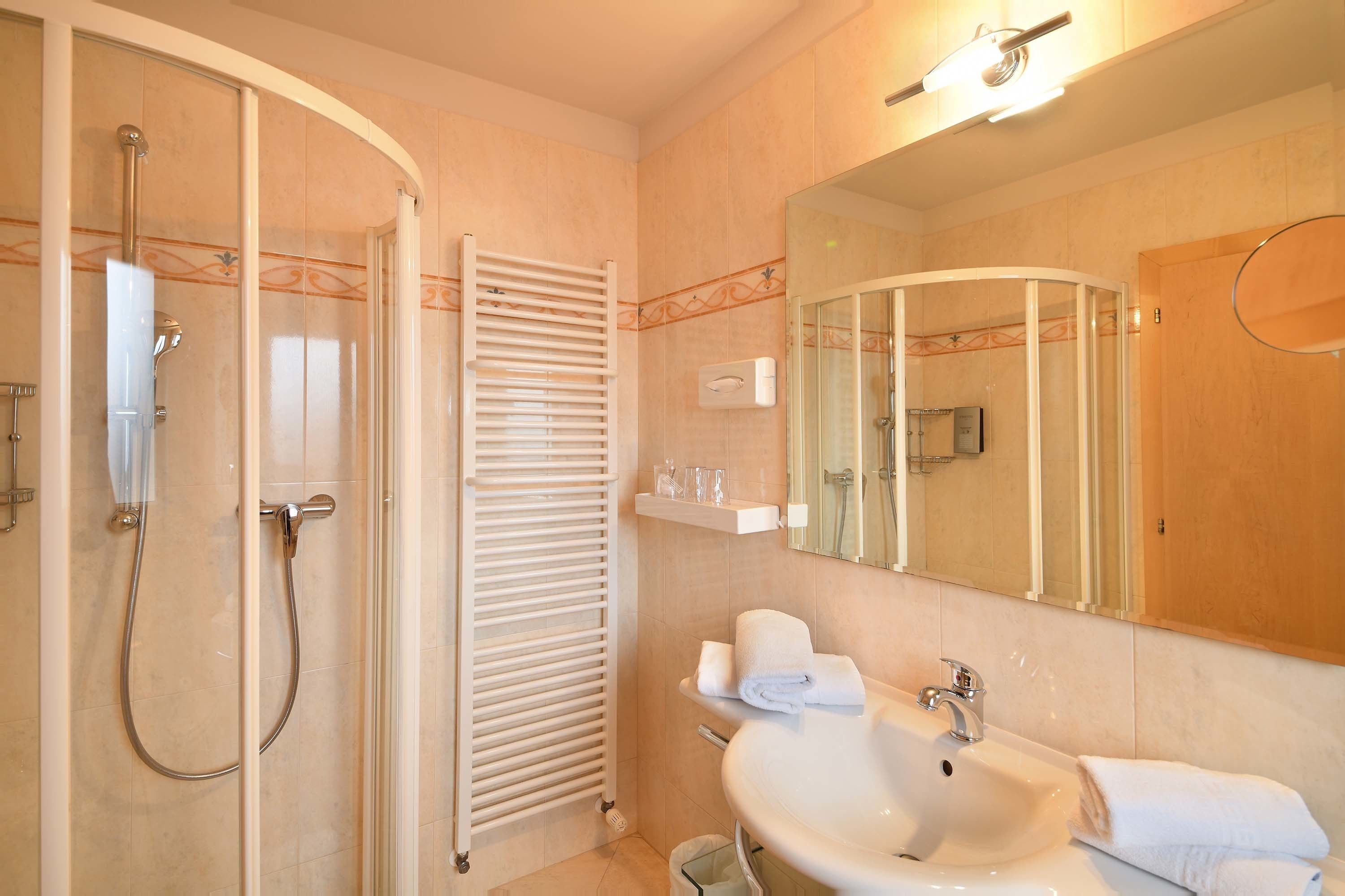 A modern bathroom with a glass-enclosed shower, a white sink, and a large mirror.