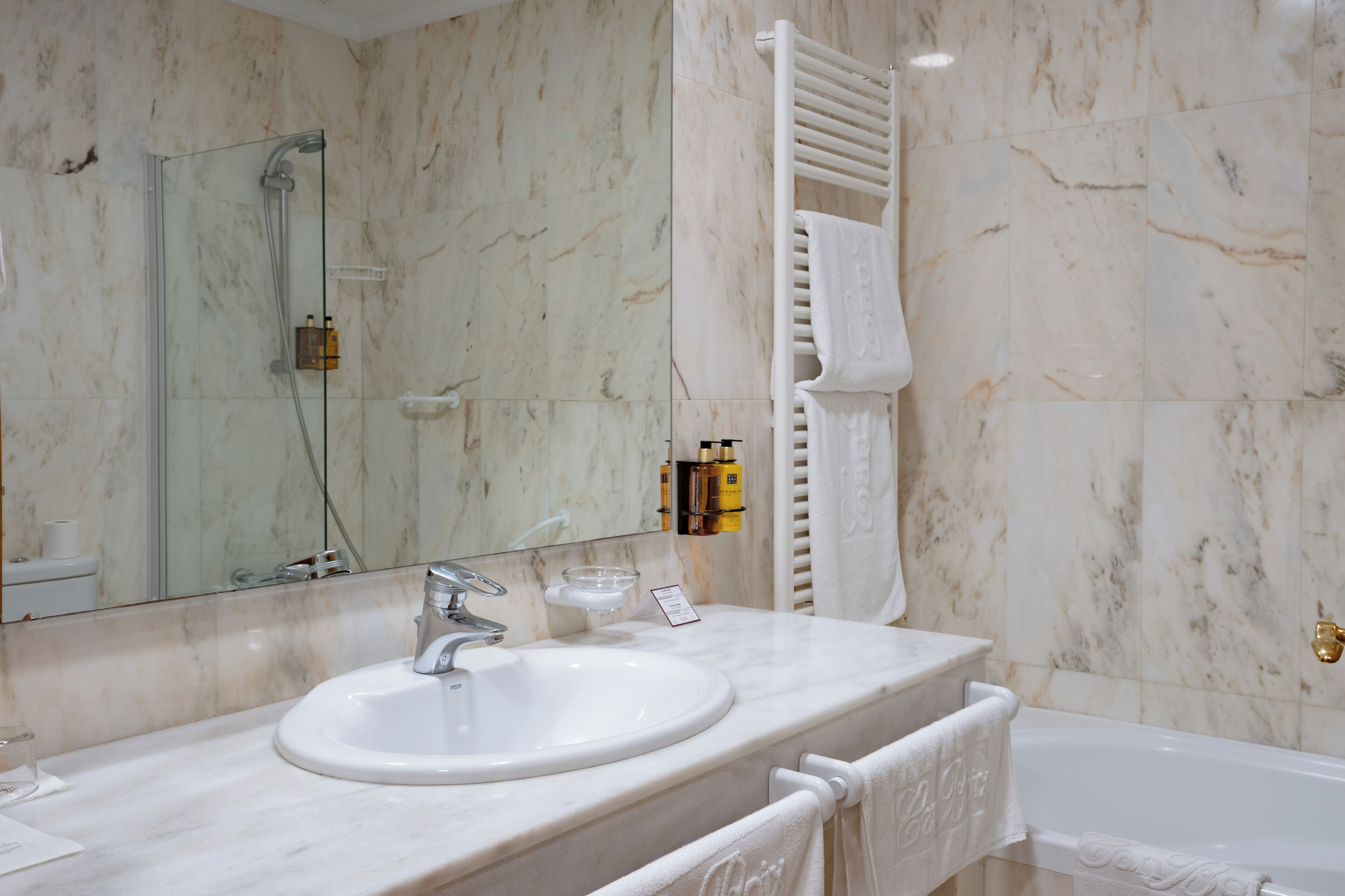 A bathroom with a marble sink, a glass-enclosed shower, and a white bathtub.