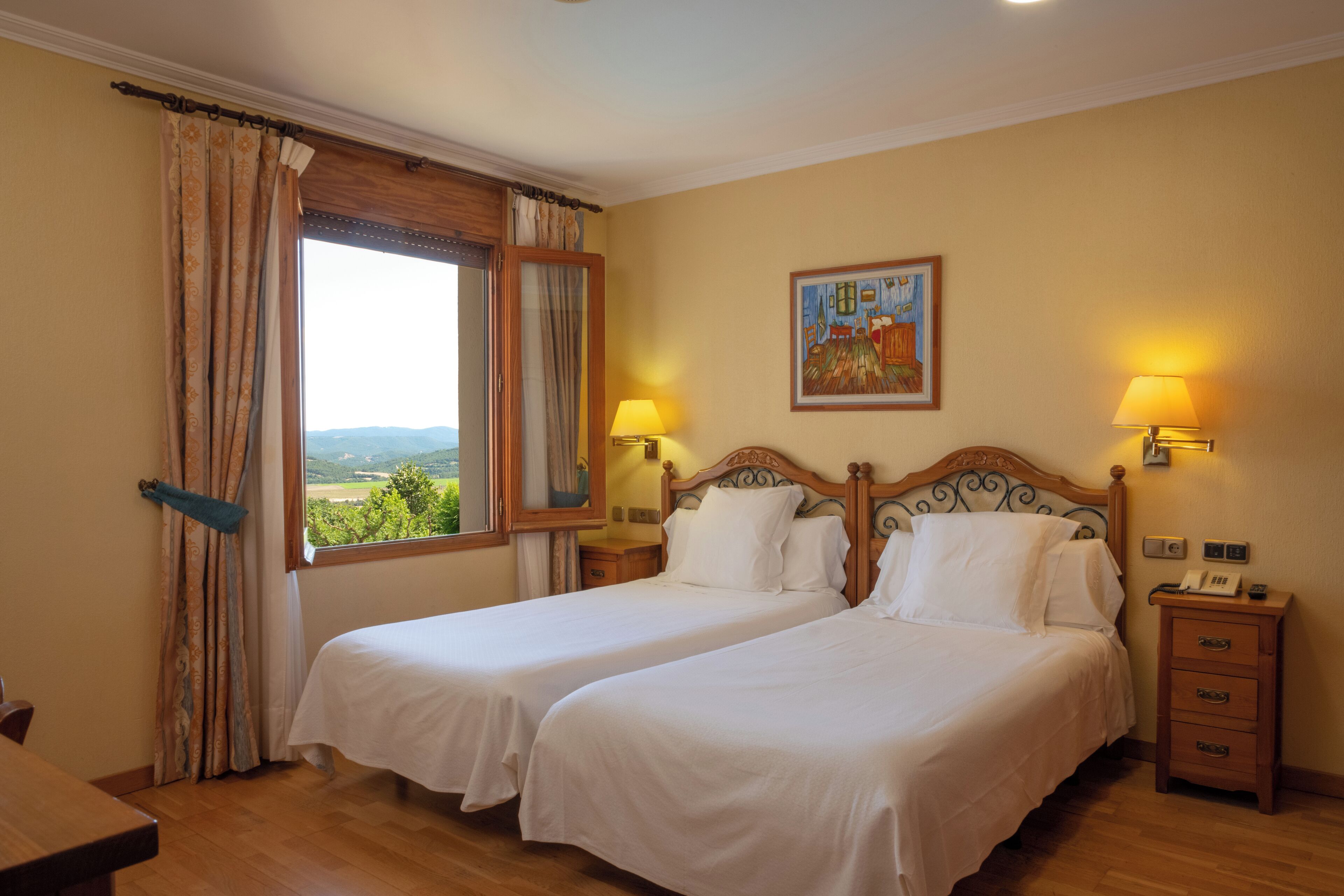 Habitación de hotel con dos camas, cabecero de madera, un cuadro en la pared y una ventana con cortinas.