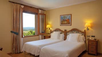 Habitación de hotel con dos camas, cabecero de madera, un cuadro en la pared y una ventana con cortinas.