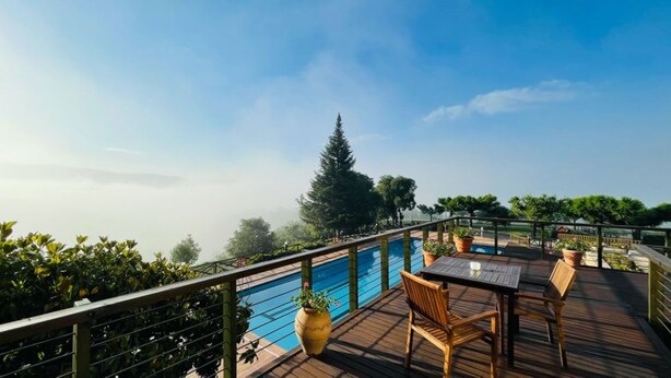 Terraza de madera con piscina, rodeada de follaje y cielo despejado.
