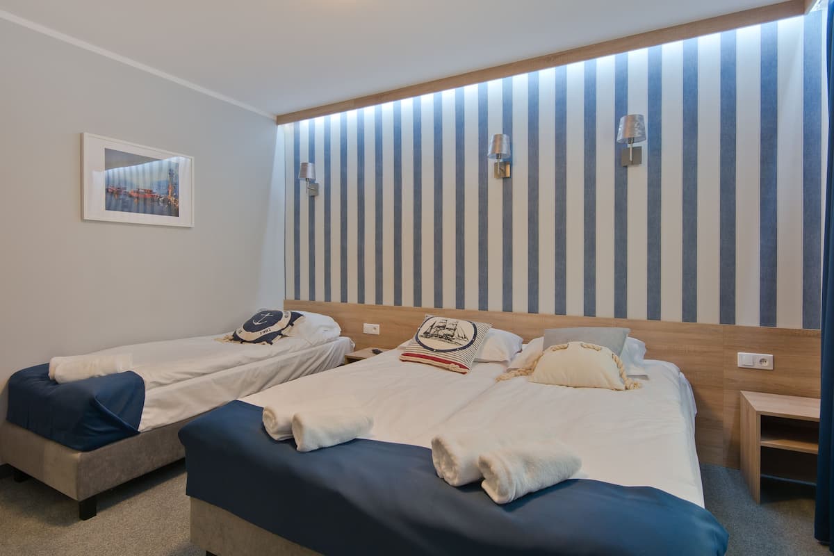 Habitación de hotel con dos camas individuales, cabecero de madera, papel tapiz a rayas, un cuadro enmarcado en la pared y lámparas de noche.