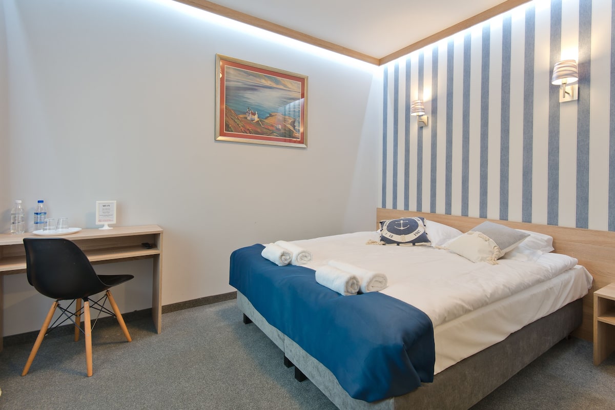 Habitación de hotel con cama, escritorio, una silla, un cuadro en la pared y dos lámparas de pared.