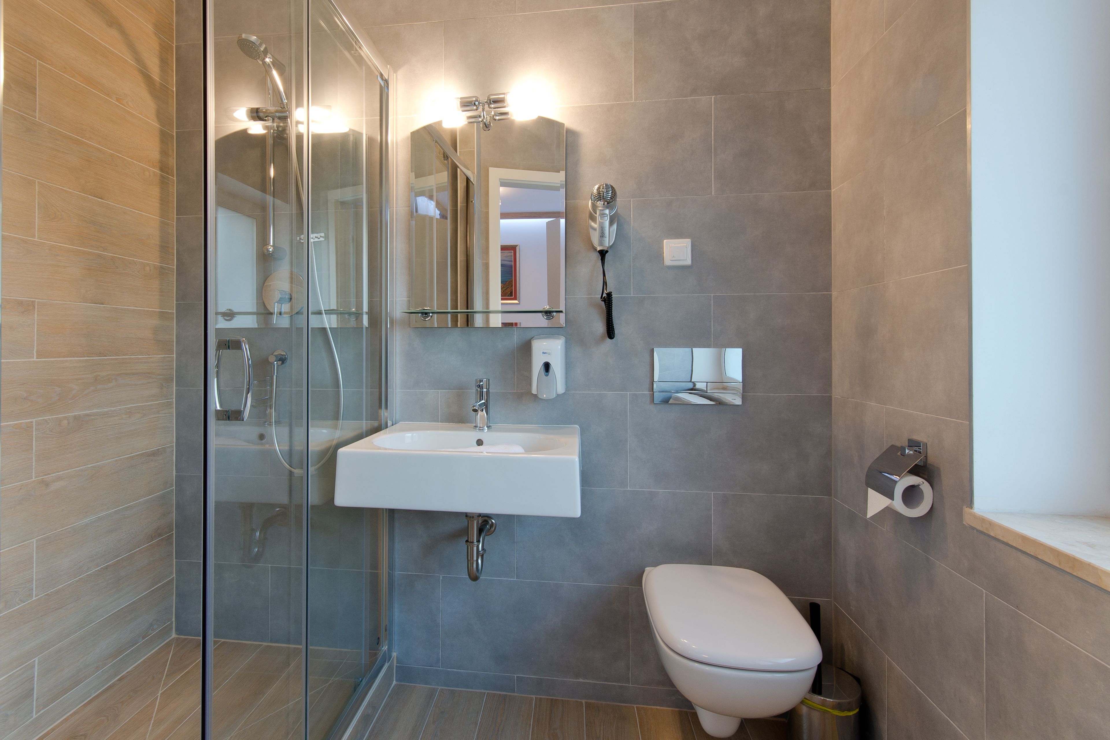 Een moderne badkamer met een douchecabine van glas, een witte wastafel en een toilet.