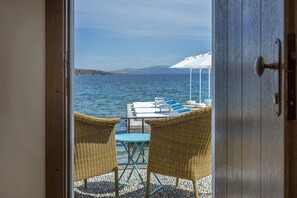 An open door leading to a balcony with wicker chairs, a table, and a view of the sea.