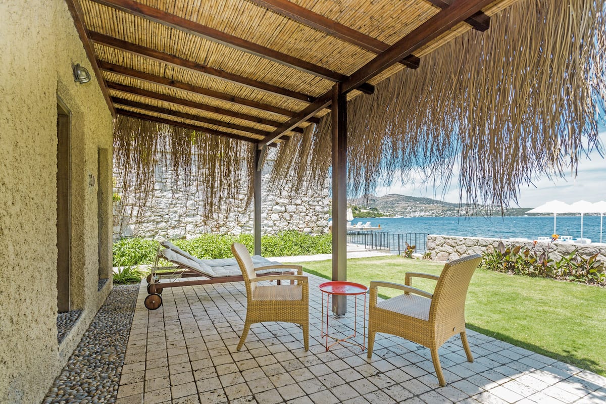 A covered patio with wicker furniture, a stone wall, and a view of the sea.