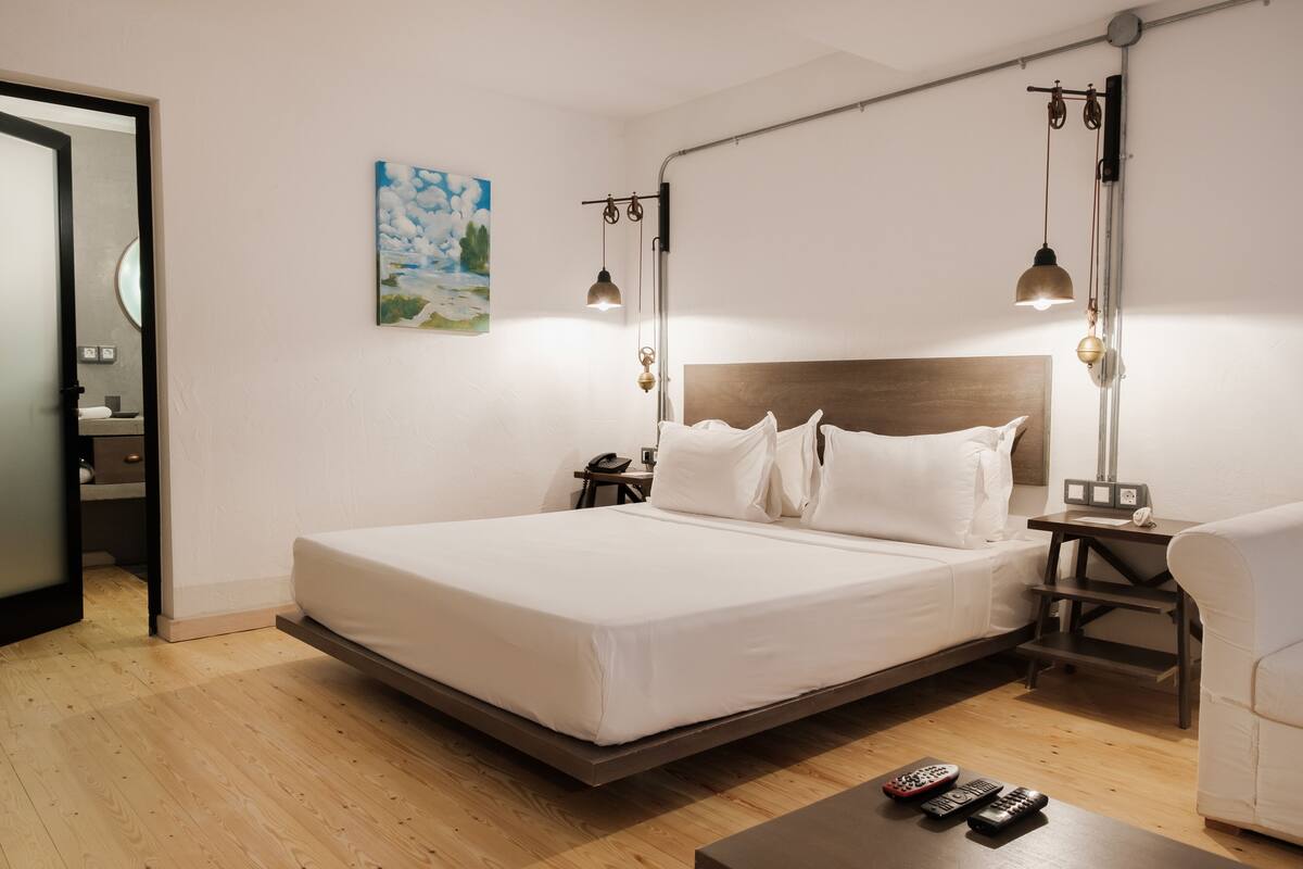 A modern hotel room with a large bed, bedside tables, a desk, and a painting on the wall.