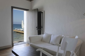 A room with a white sofa, a wooden table, and a view of the sea through an open door.