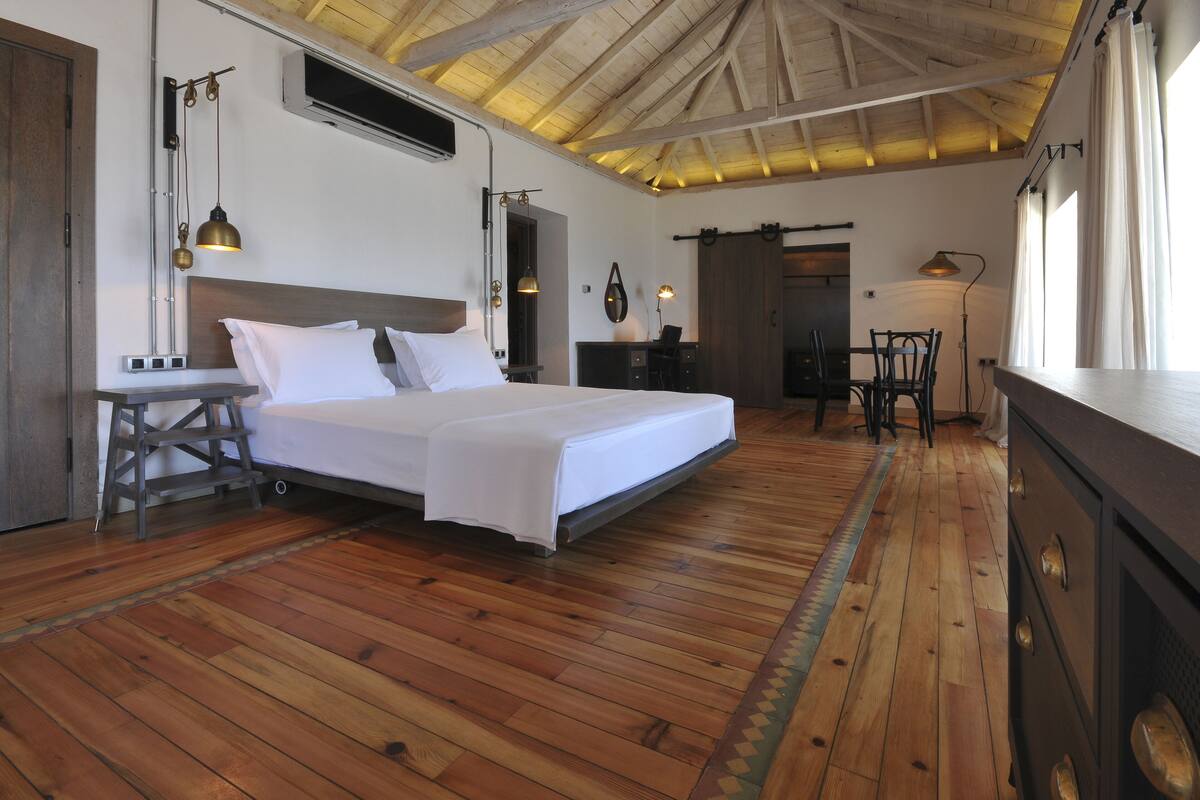 A spacious bedroom with a large bed, wooden flooring, and a ceiling with exposed beams.