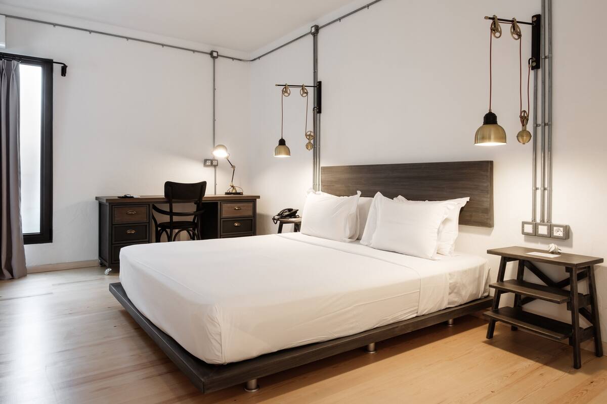 A modern bedroom with a large bed, a desk, and a chair. There are two bedside tables with lamps.