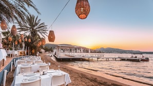 Un restaurante frente al mar con mesas dispuestas para comer, con vista al océano y al atardecer.