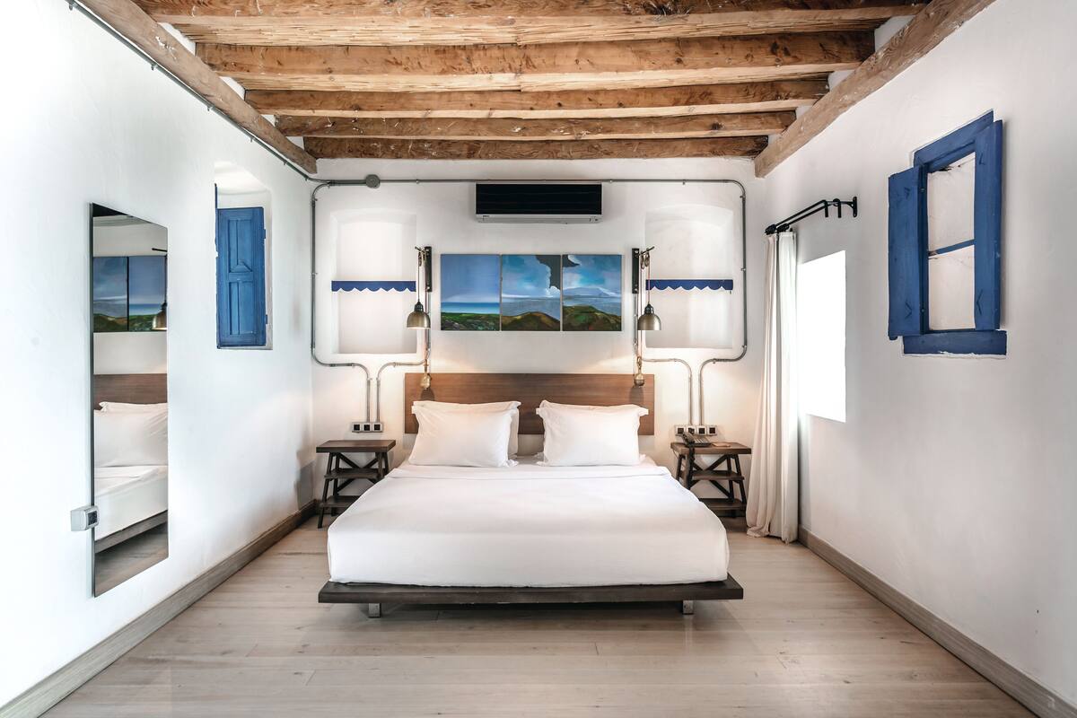 A bedroom with a wooden ceiling, a bed with white bedding, two bedside tables with lamps, and a window with curtains.