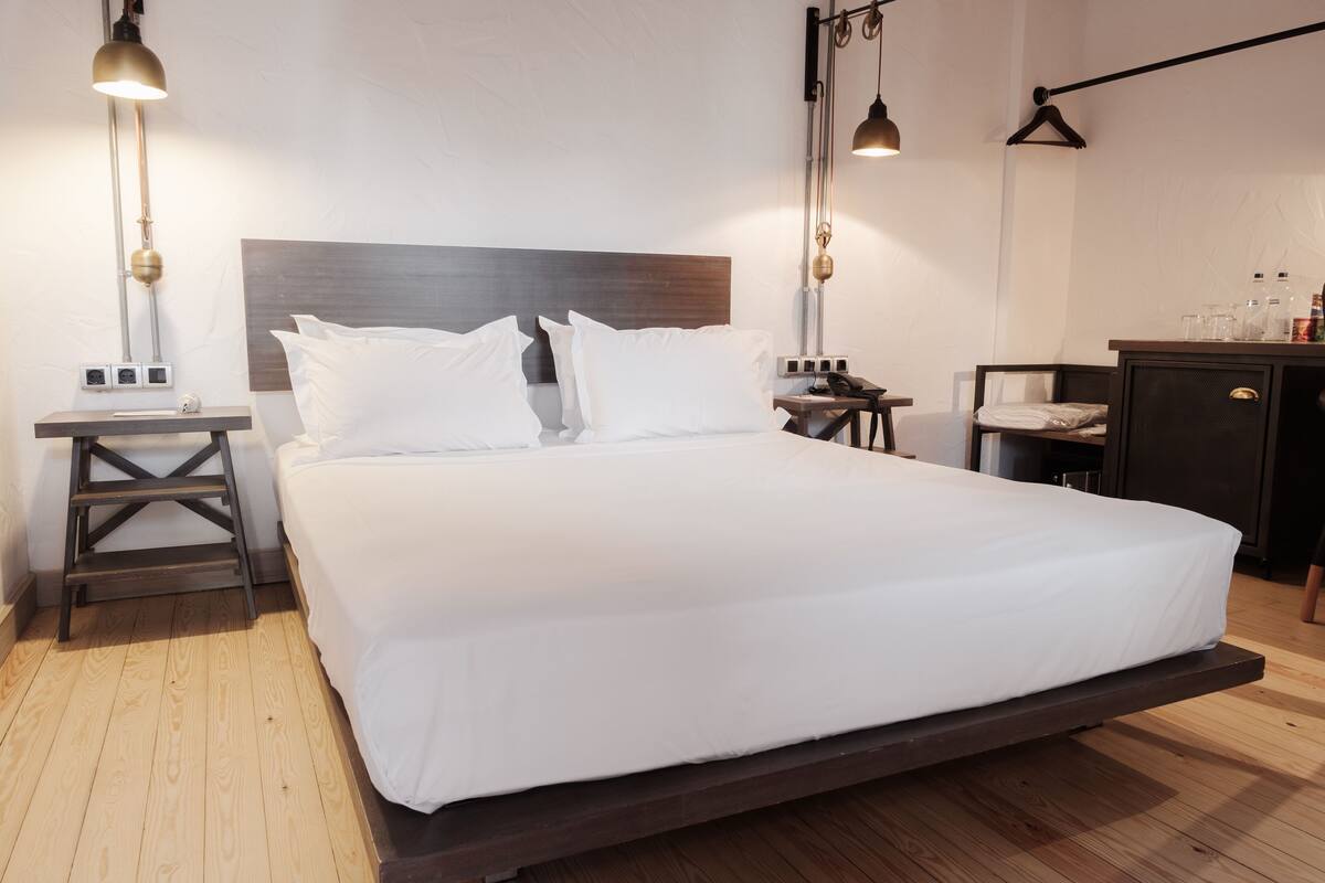 A modern bedroom with a large bed, wooden floor, and a desk with a chair.