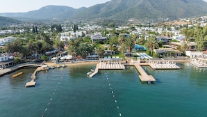 Vista aérea de un complejo turístico costero con un puerto deportivo, sombrillas de playa y una zona de piscina.