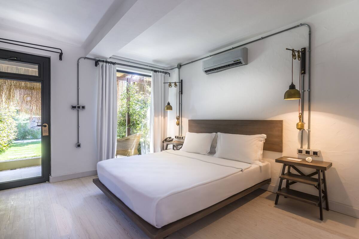 A modern bedroom with a large bed, an air conditioning unit, a desk, and a chair.