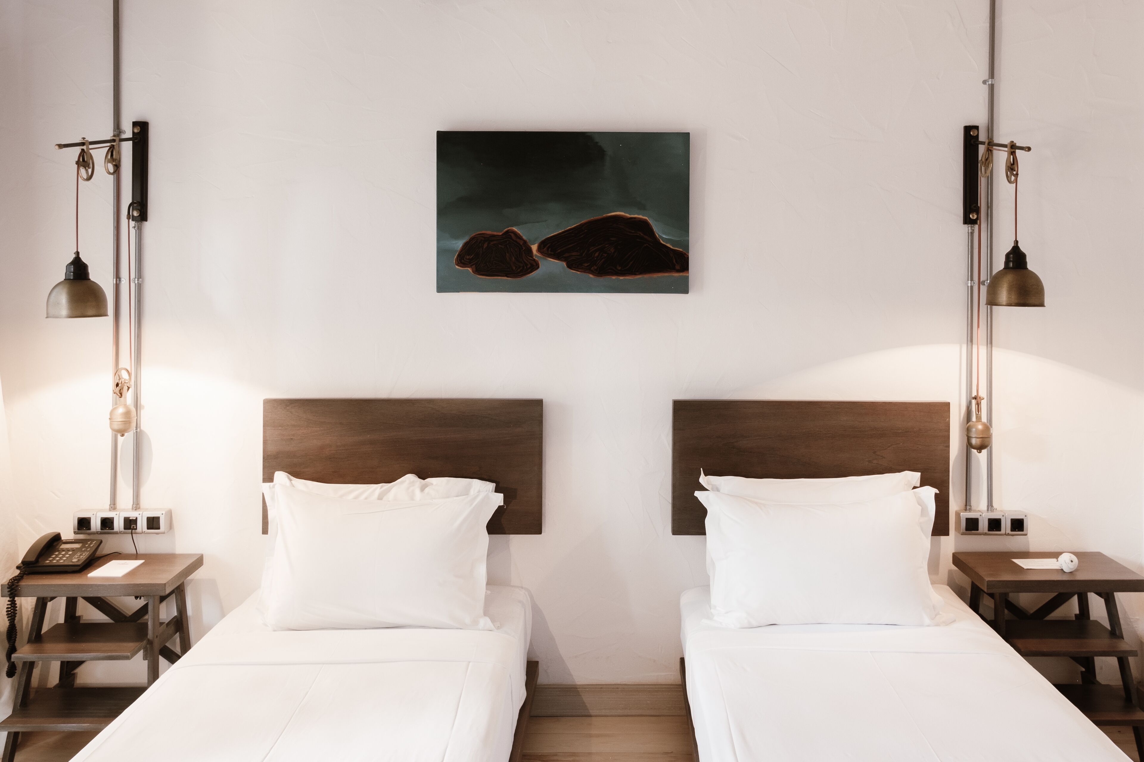 A hotel room with two beds, a nightstand with a phone, and a wall-mounted artwork.