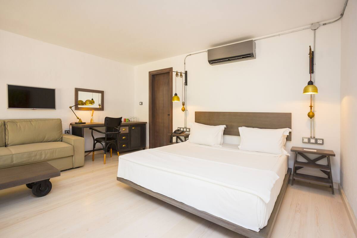 A modern hotel room with a large bed, a desk, a sofa, and a TV.