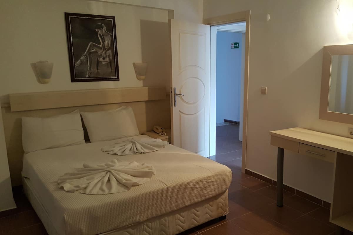 A hotel room with a bed, a bedside table, a mirror, and a door leading to another room.