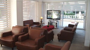 A living room with leather sofas, a TV, and a table with a lamp. - Golden Star Otel (Marmaris)